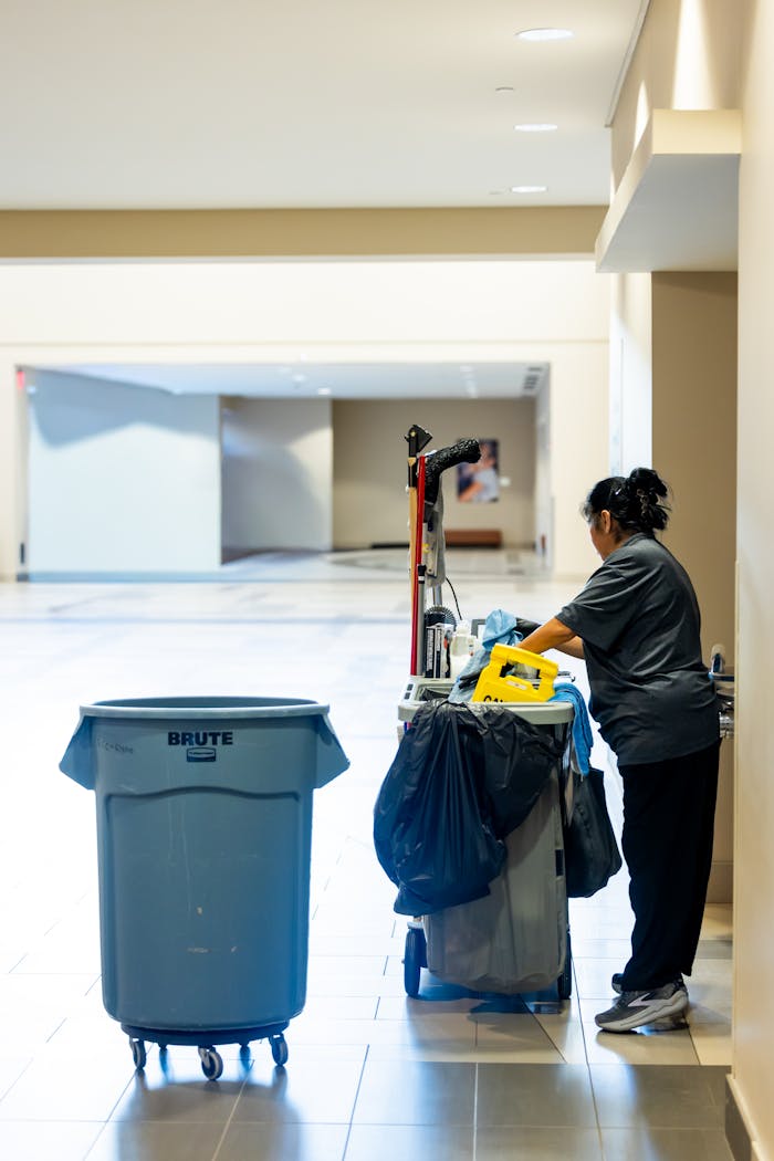 gallery-05 A janitorial worker pushes a cleaning cart in a spacious indoor hallway.